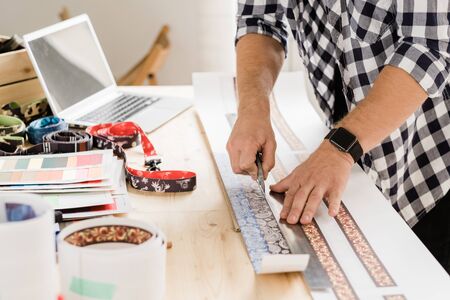 Young casual craftsman with knife and ruler bending over table while cutting decorative workpieces for creative pet collarsの写真素材