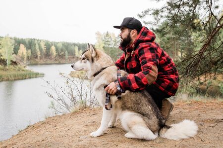 Young bearded man in casualwear embracing husky dog during chillの写真素材