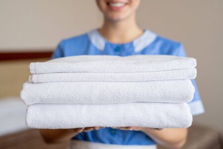 Stack of white clean soft towels held by young smiling housewife or chambermaidの写真素材