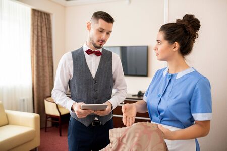 Young pretty room maid looking at porter while showing him stain on blanketの写真素材