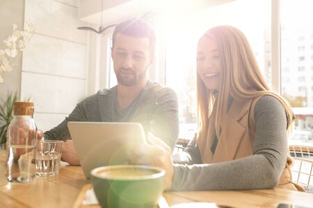 Happy young blond woman and her boyfriend using touchpad in cafeの写真素材