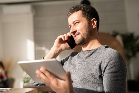 Busy agent in casualwear consulting client on mobile phone and using touchpadの写真素材