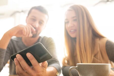 Young man holding smartphone while showing curious stuff to his girlfriend