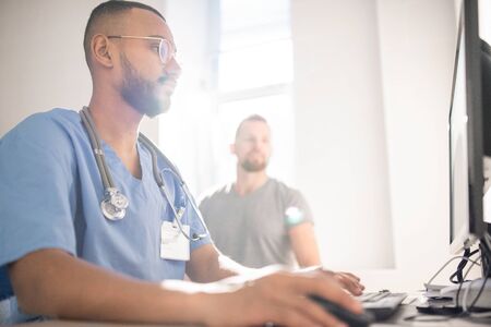 Serious doctor filling in electronic document with data of patient by computerの写真素材