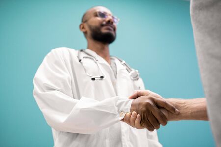 Handshake of young successful clinician in whitecoat and his recovered patient after medical consultation in hospitalの写真素材