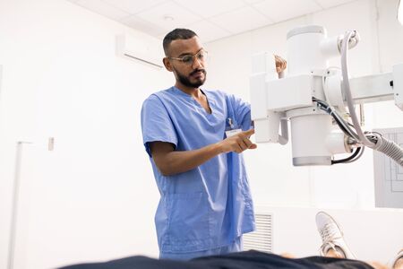 Bearded young mixed-race man in blue uniform using new medical equipmentの写真素材