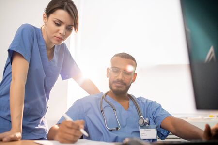 One of young clinicians showing his notes to colleague during discussionの写真素材