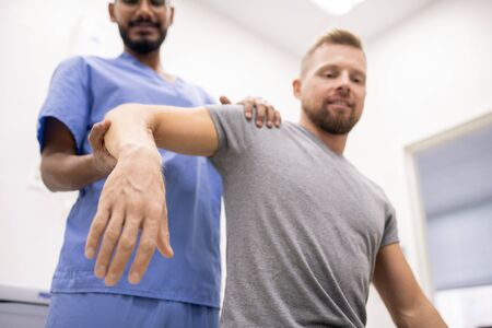 Masseur in blue uniform holding sick arm of patient while massaging it