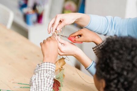 Hands of young teacher holding stick with decorations hanging on threads