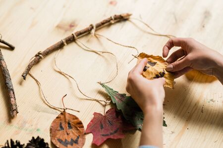 Hands of woman hanging dry leaves with drawn faces on stick over wooden tableの写真素材