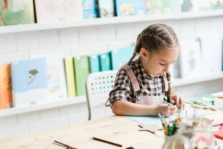 Diligent schoolgirl drawing Christmas picture by desk while working individuallyの写真素材