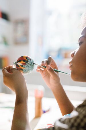Diligent mixed-race boy painting handmade decorative toy ball for Christmasの写真素材