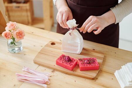 Hands of woman decorating paper packet with flowers while packing handmade soap