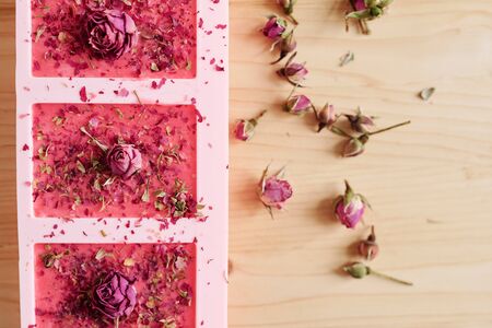 Overview of silicone molds filled with handmade pink soap sprinkled by grated dry floral petals with small rosebuds on top and near byの写真素材