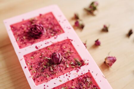 Silicone molds filled with handmade soap sprinkled by grated dry floral petals with small pink rosebuds on topの写真素材