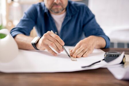 Hands of modern engineer with pencil and ruler drawing line on blueprint