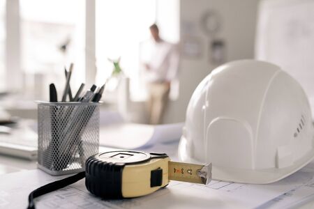 Workplace of engineer with hardhat, measuring tape, bunch of pencils and sketchの写真素材