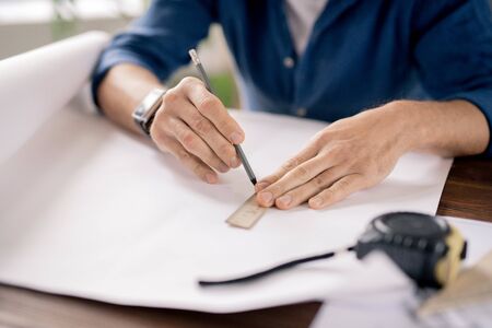 Hands of mature engineer holding pencil and ruler while drawing line on blueprint and making sketch of constructionの写真素材