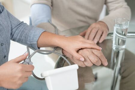 Hands of young woman with tonometer measuring blood pressure of her sick father