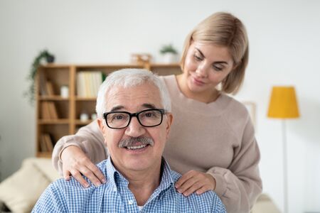 Careful young woman doing massage of shoulders to her senior father at home