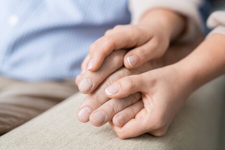 Hands of affectionate and careful daughter holding that of her senior fatherの写真素材