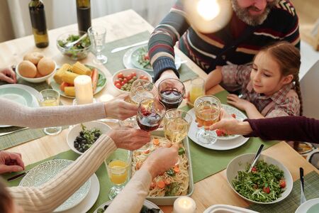 Hands of family of six clinking with drinks over festive table homemade foodの写真素材