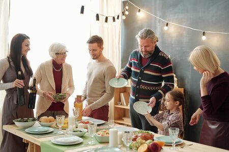 Family of five taking plates for snacks and preparing drinks before celebration