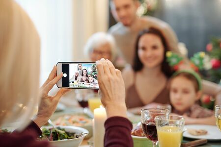 Hands of mature female holding smartphone while taking photo of her familyの写真素材