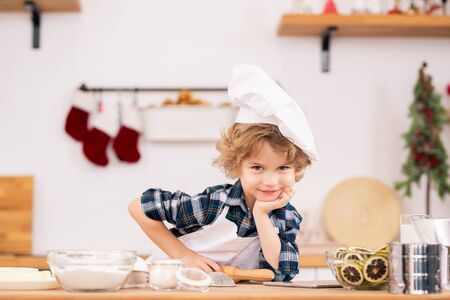 Cute little boy in apron and chef hat holding rolling-pin and looking at youの写真素材