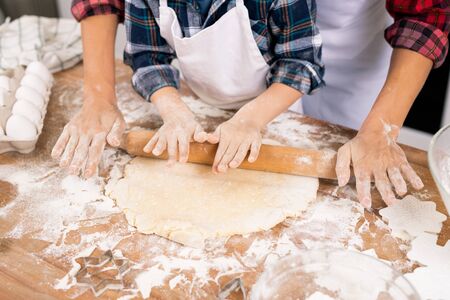 Hands of young female and little boy rolling dough while preparing cookies