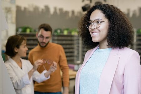 Happy young mixed-race female in eyeglasses standing in front of mirrorの写真素材