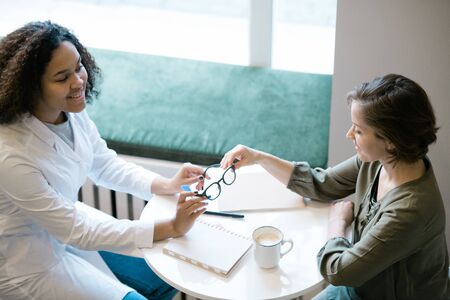 Young clinician in whitecoat consulting patient or client about new eyeglassesの写真素材