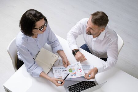Young female financier and her colleague discussing financial papers