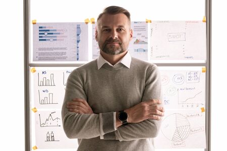 Casual mature businessman standing against whiteboard with documents