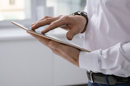 Hands of elegant businessman with tablet scrolling through online data
