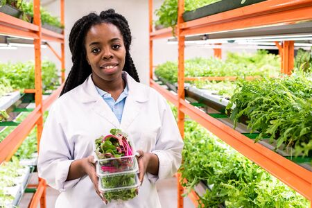 Young smiling female greenhouse worker with stack of containersの写真素材