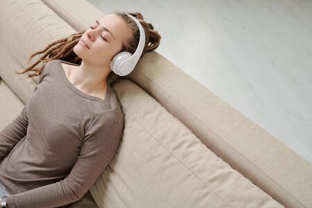 Cute female enjoying music for relax while sitting on comfortable couch