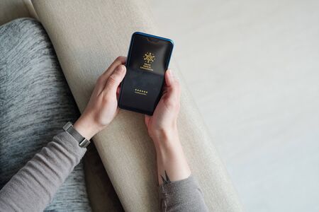 Hands of girl with mobile phone sitting on couch and waiting for loading profile