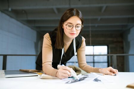 Creative young female designer pointing at on of fashion sketches at work