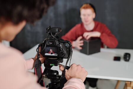 Hands of young operator by camera shooting contemporary male vlogger
