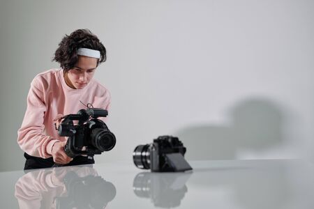 Young serious video blogger standing in front of new photo equipment on deskの写真素材