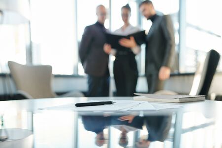 Pen on papers and notebook on background of business partners looking through documents at meetingの写真素材