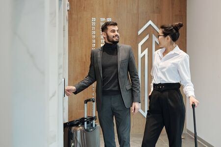 Intercultural business travelers interacting by one of elevator doors in hotel