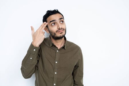 Perplexed young man in casualwear holding two fingers by his head