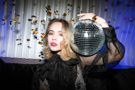 Pretty young blond female in black evening dress holding glittering disco ballの写真素材