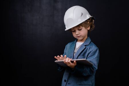 Serious cute little boy in hardhat and formalwear using digital tabletの写真素材