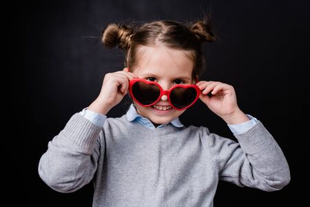 Cheerful girl with toothy smile taking off stylish sunglasses and looking at you