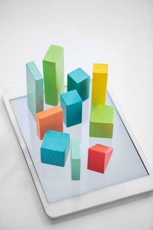 Blue, orange and green flat wooden bricks and cubes symbolizing chart on touchpad screen over white backgroundの写真素材