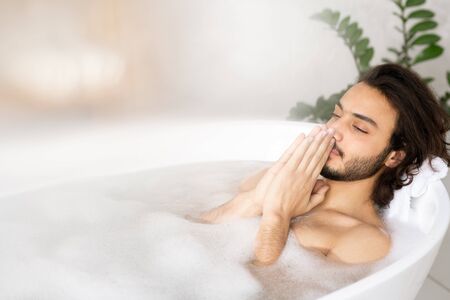 Young serene man meditating while enjoying hot bath with foam