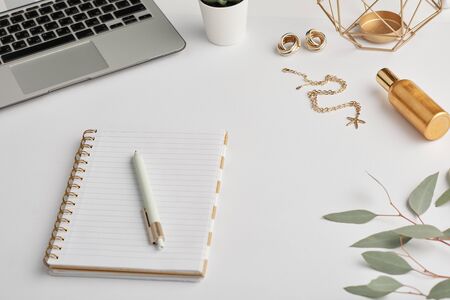 Gold earrings and chain, notebook with pen, bottle of scent and laptop keypad on white desk that is workplace of employeeの写真素材